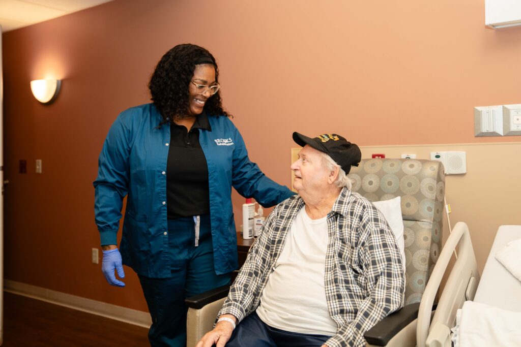 A nurse talks with an elderly patient in a hospital room.