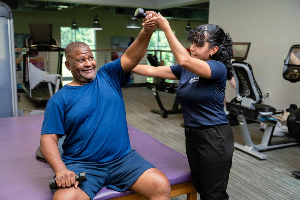 Therapist helping patient on with dumbbell and arm raised