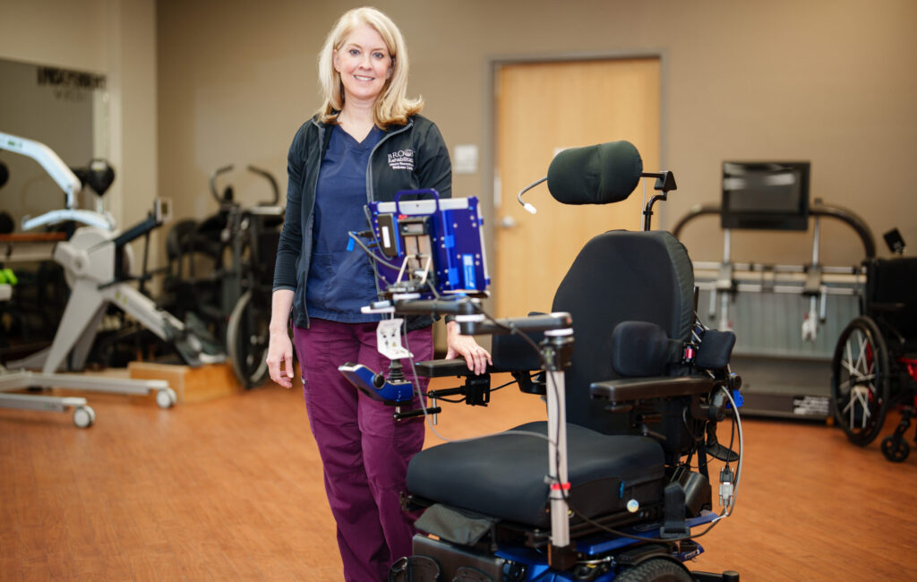 Staff member standing near a wheelchair hooked up to a monitor