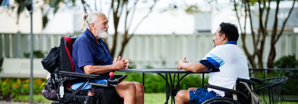 A man in a wheelchair sits at a table with another man in Brooks Peer Mentorship program.