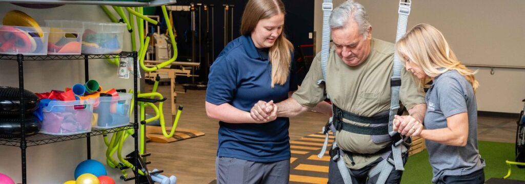 Two physical therapists in the SCI Day Program help a patient walk with a Zero gravity harness.