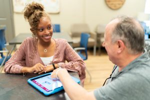 Student helping patient at brooks rehab to navigate a loss of language caused by a stroke or brain injury in a device.