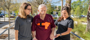 Man walks with his neuro team at Brooks Rehabilitation