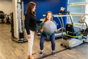 Young woman exercises with large ball and physical therapist