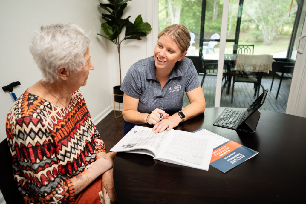 Home health aide discusses services with a woman at her dining room table.
