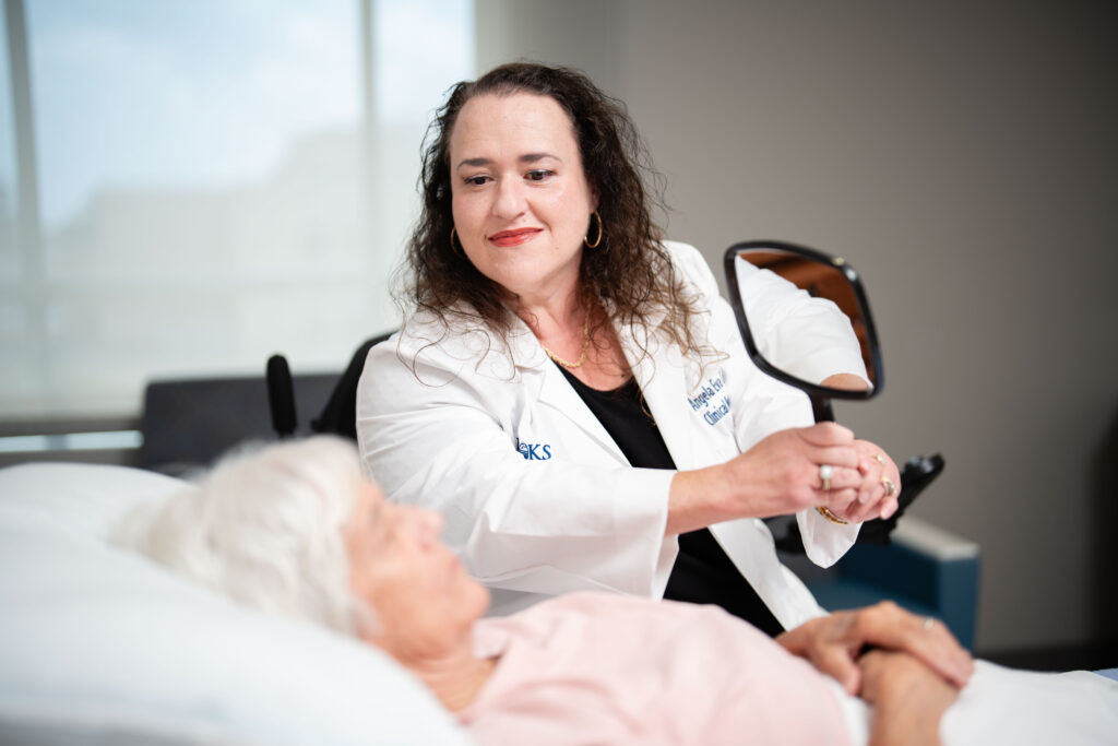 A Neuropsychologist holds a hand mirror up to a DoC patient in a hospital bed.