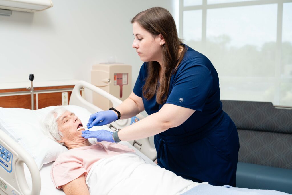 A speech therapists brushes a patient's mouth while they are in their hospital bed.