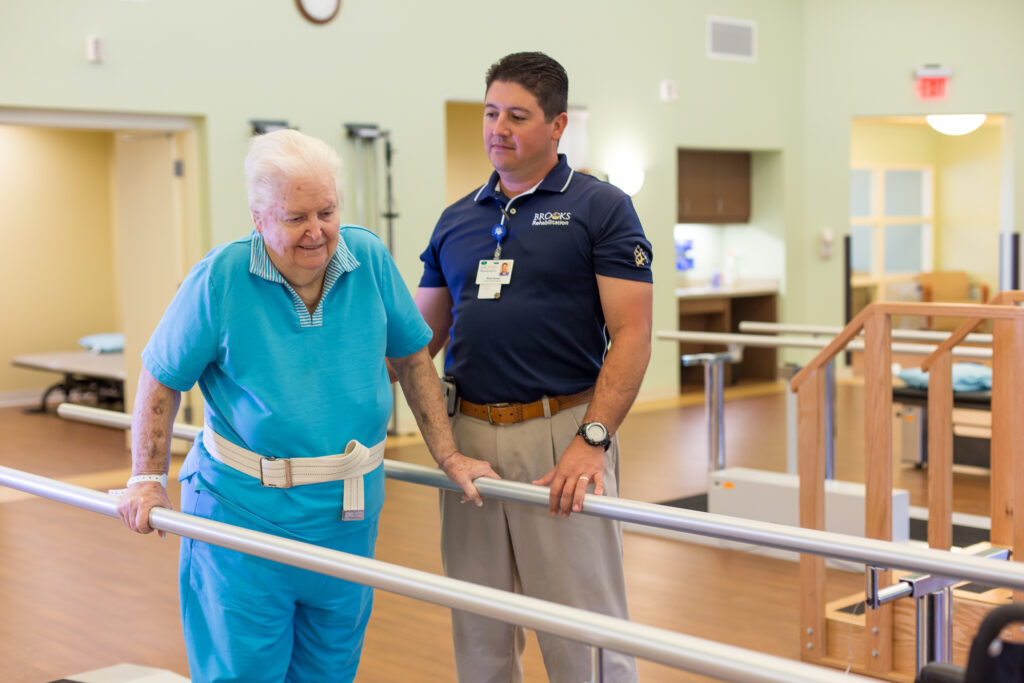 A Brooks Rehabilitation stands by while a woman walks in physical therapy