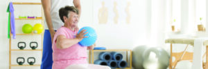 A senior woman excercises with ball and therapist