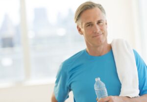 Man in exercise wear holding a water bottle and towel while looking at the camera