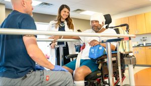 Dr. List and staff member talking to a patient in a chair on a track