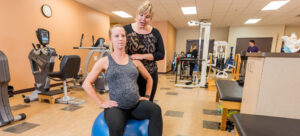 Pregnant patient sitting on an exercise ball and talking to Brooks staff