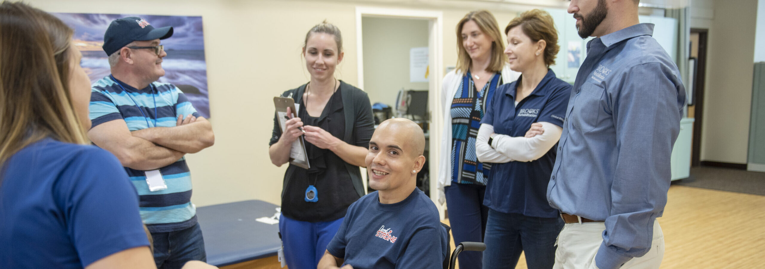 Patient in wheelchair smiling at the camera surrounded by Brooks staff