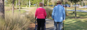 A woman with a walker and a man with a cane walk away from the camera