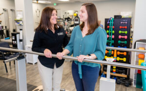 Physical therapy patient gripping balance beam while talking to staff member