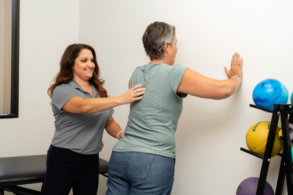 a physical therapist specializing in oncology PT assists a patient doing wall push ups.