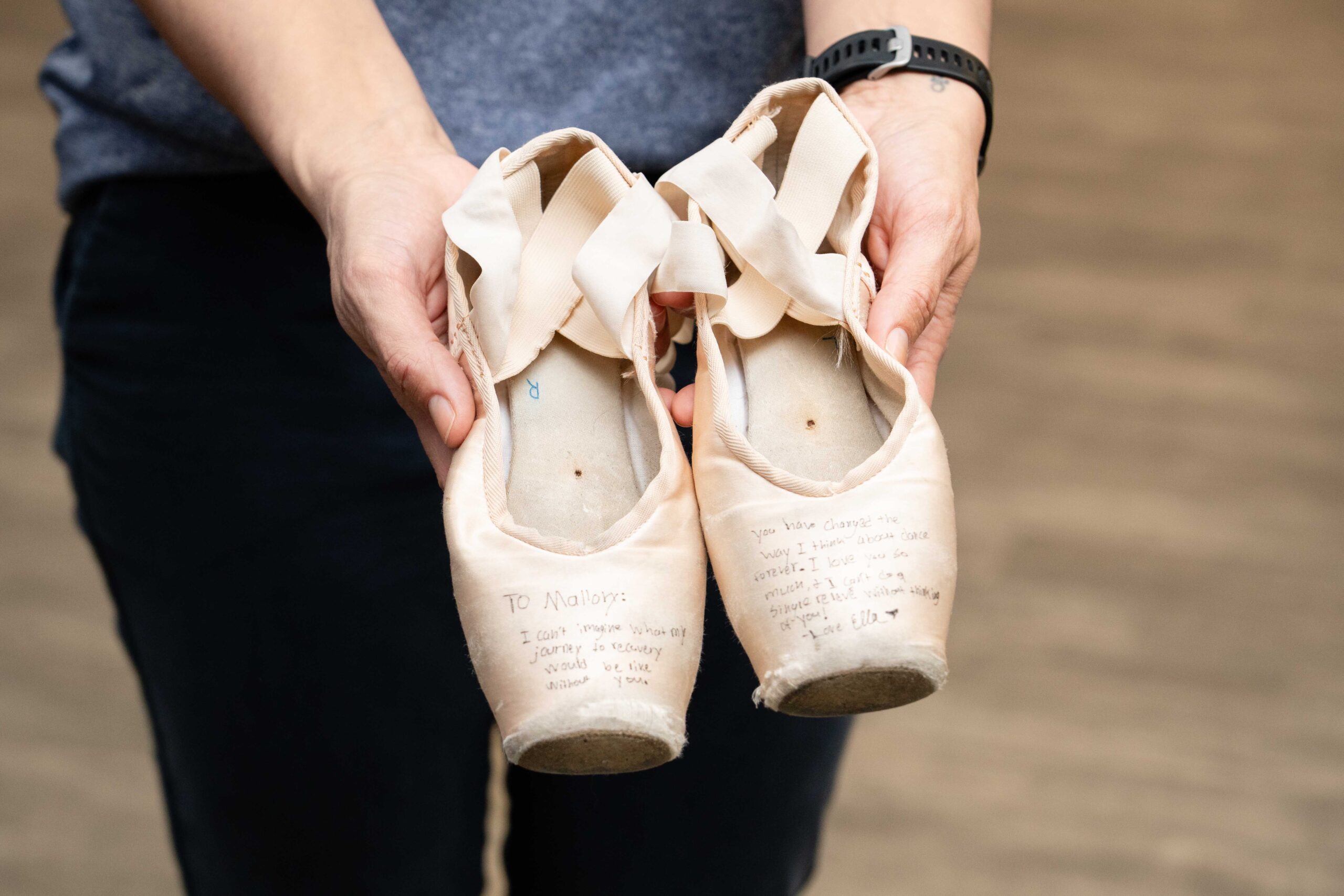 a pair of pink ballet dance shoes being held in Mallory Behenna's hands