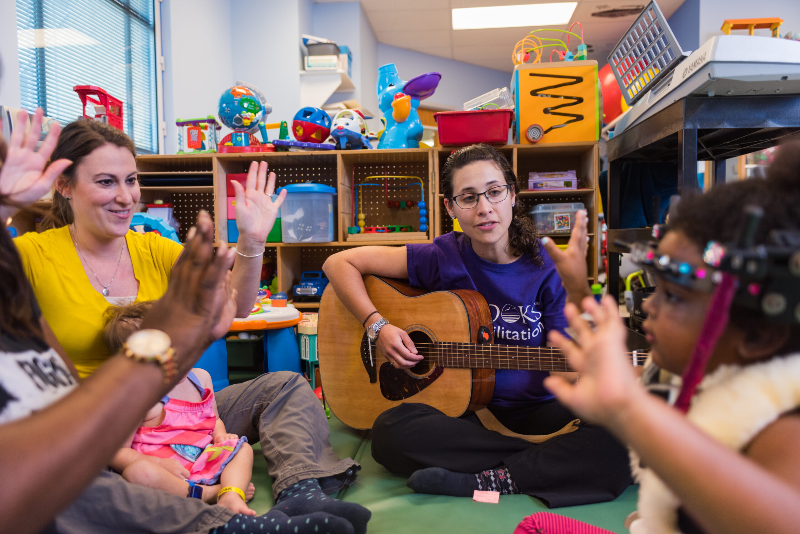 music therapist danielle porter sits on the floor in the pediatric gym leading a song circle with patients. 