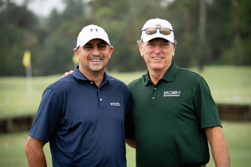 Two men wearing brooks logoed attire standing on the golf course.