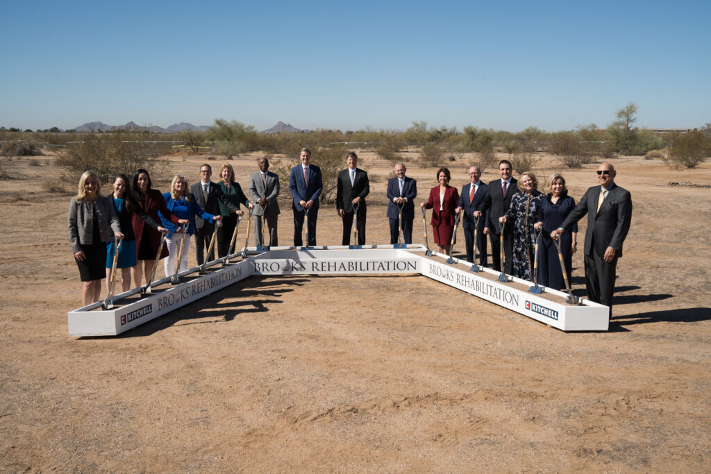 Leaders at Brooks and Mayo Clinic line up with shovels in hand in a desert terrain.