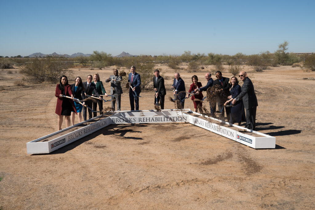 Leaders at Brooks and Mayo Clinic scoop up dirt with shovels in the desert.