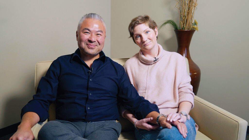 Lindsey Song sits on a couch with husband talking about her recovery journey.
