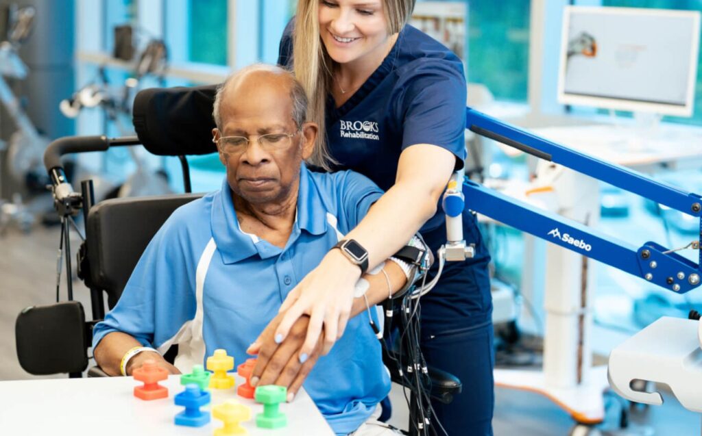 An occupational therapist helps a male elderly patient grip colorful pieces of rubber to work on motor skills.
