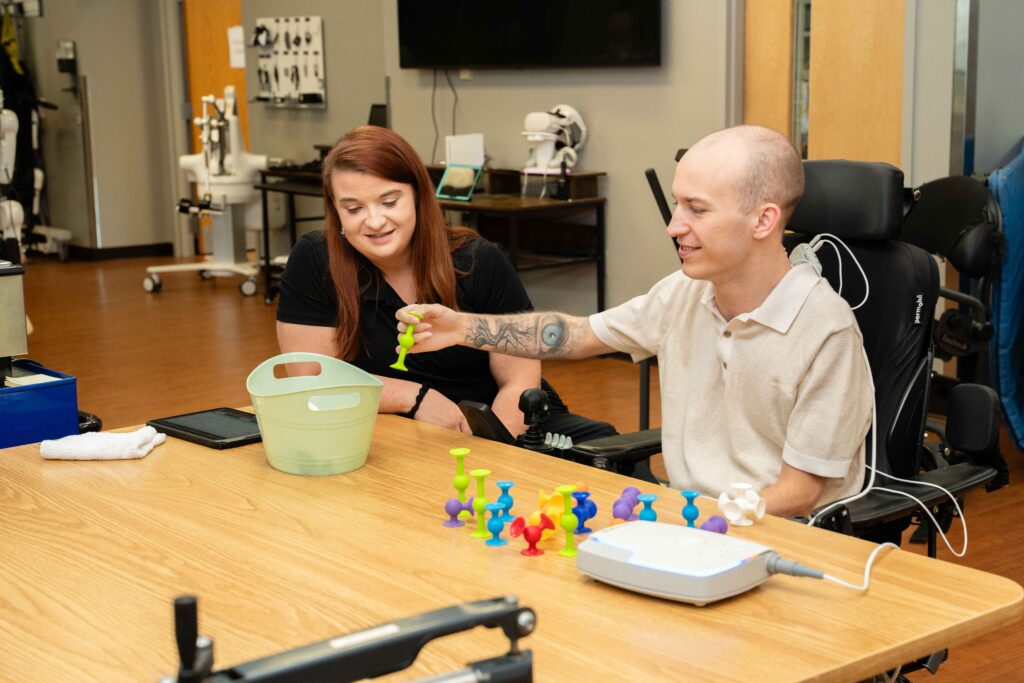 sci patient works with a therapist on picking up items while using arc-ex.