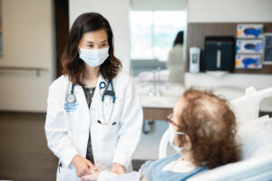 Dr. Lee at patient's bedside holding her hand and talking to her