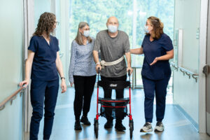 Transplant patient walking with therapists with walker in the gym