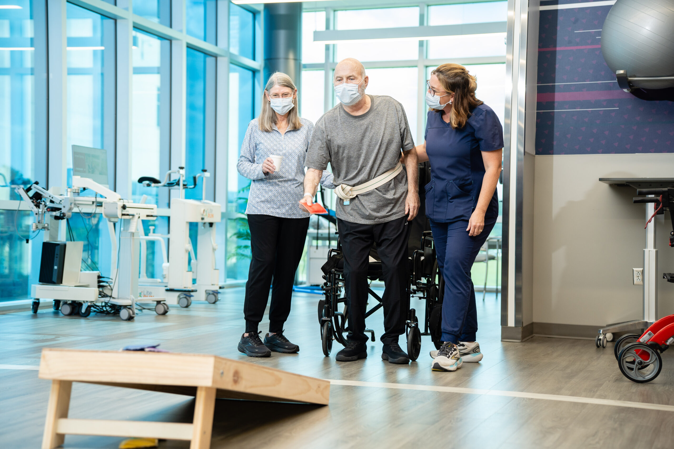 Transplant patient playing cornhole with therapists in therapy gym