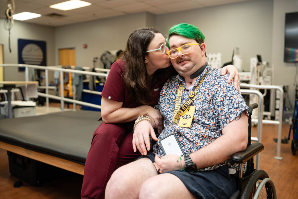 Kesley kissing Nick on the cheek sitting in therapy gym
