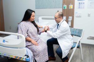 a physician performs a strength assessment on a woman patient in a hospital gown by having her push on his hand.