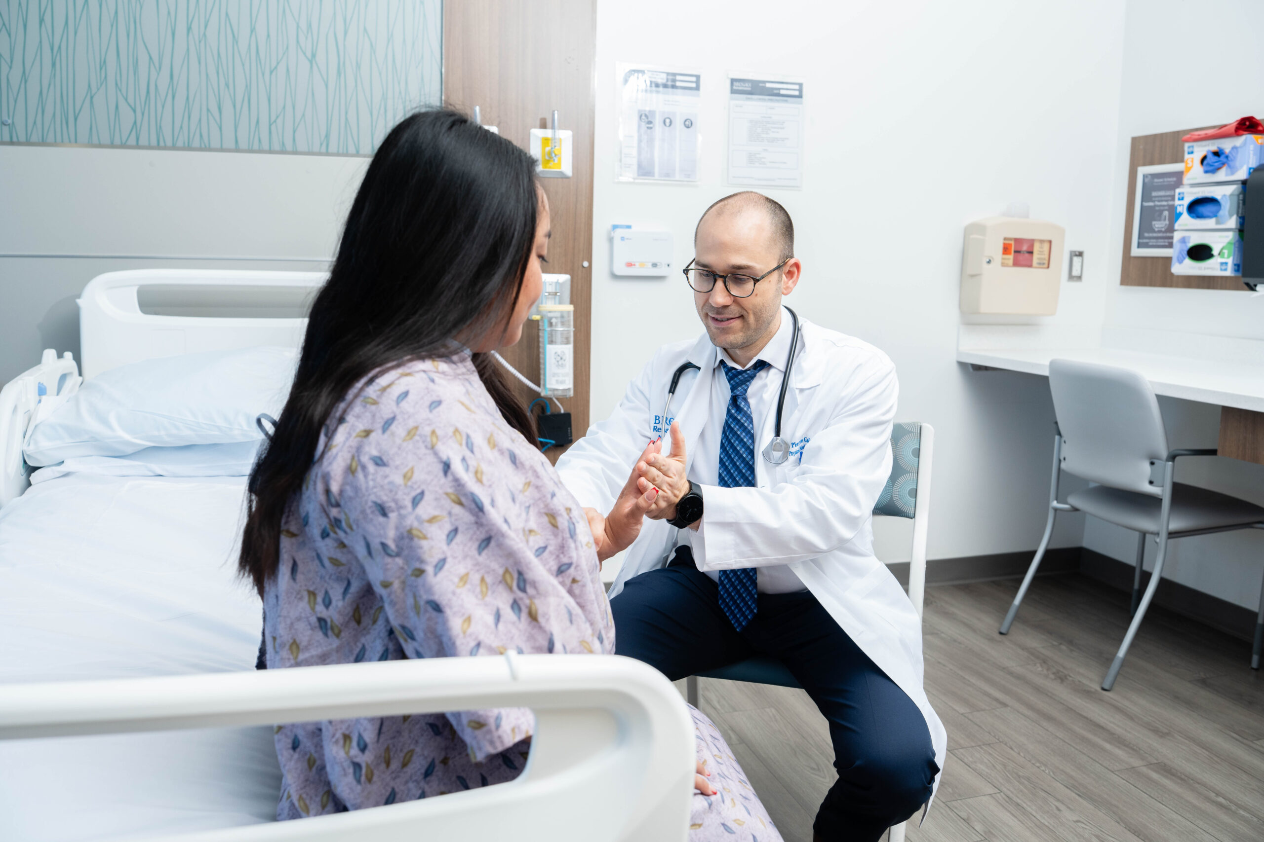 a physician performs a strength assessment on a woman patient in a hospital gown by having her push on his hand.