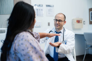 a physician performs a strength assessment on a woman patient in a hospital gown by having her push on his hand.