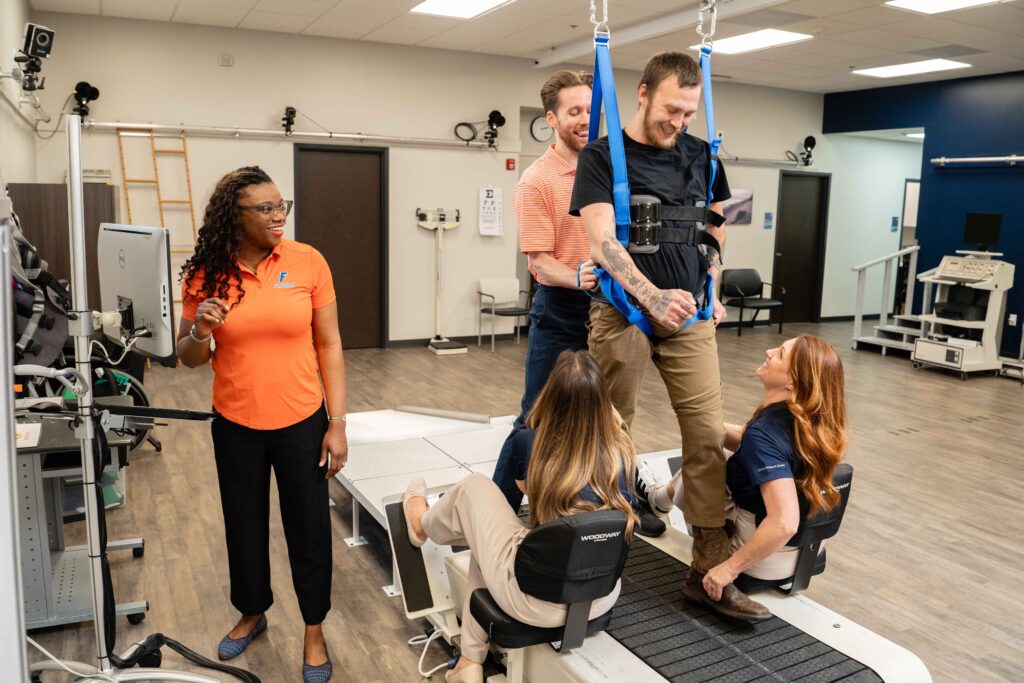 A group of research students from UF and Brooks clinicians support a spinal cord injury research participant on a treadmill.