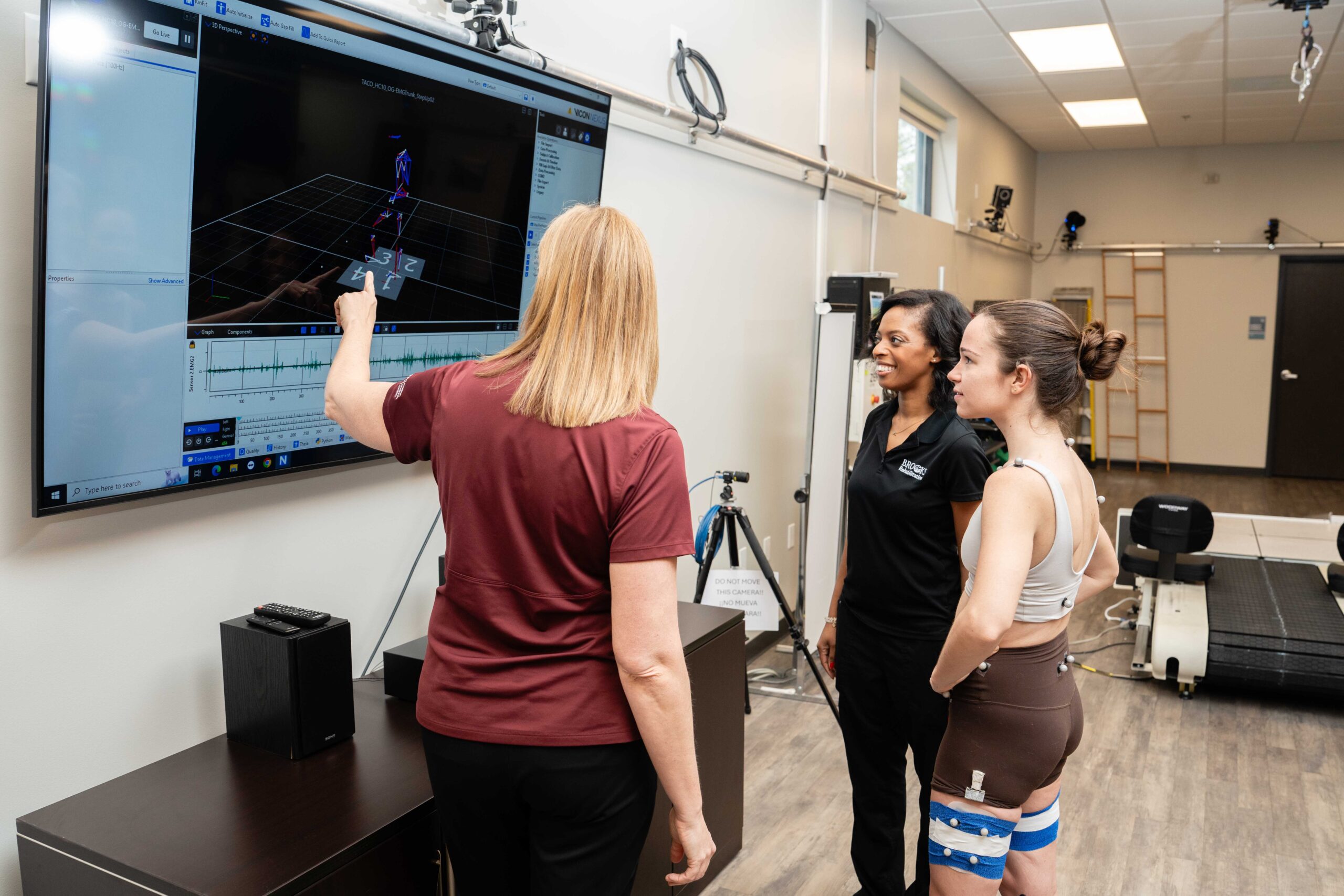 Two Brooks clinicians point to a large screen demonstrating movement data of a young female research participant.