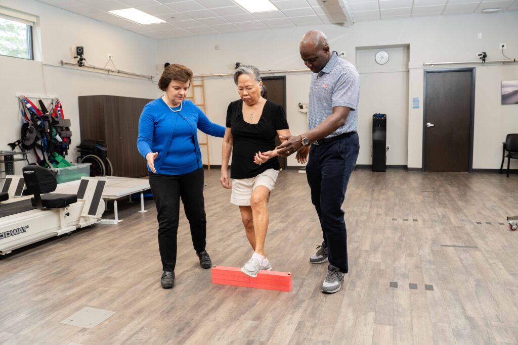 A Brooks researcher and research student at UF PHHP, support a woman stroke research participant as she steps over brightly colored blocks.