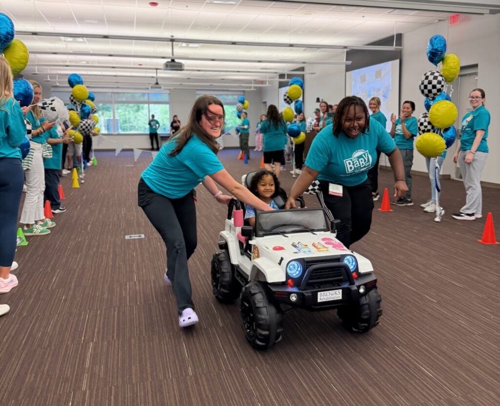 Child in car for GoBabyGo being pushed by two volunteers