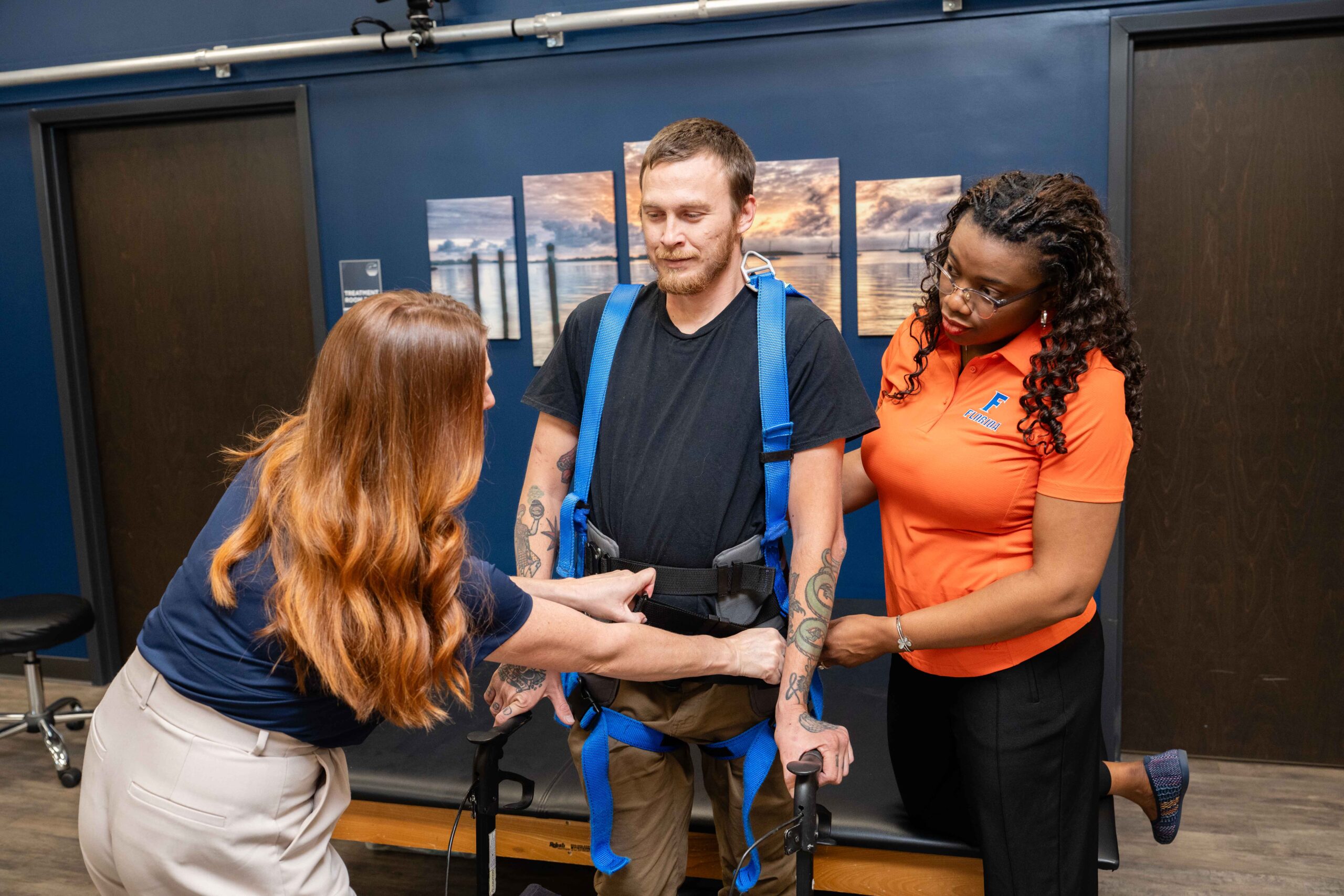 Brooks clinician and a research student assist male spinal cord injury participant into a harness for the treadmill.