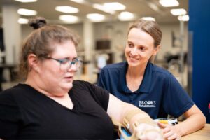 A therapists splits a female patient's arm at an outpatient clinic gym.